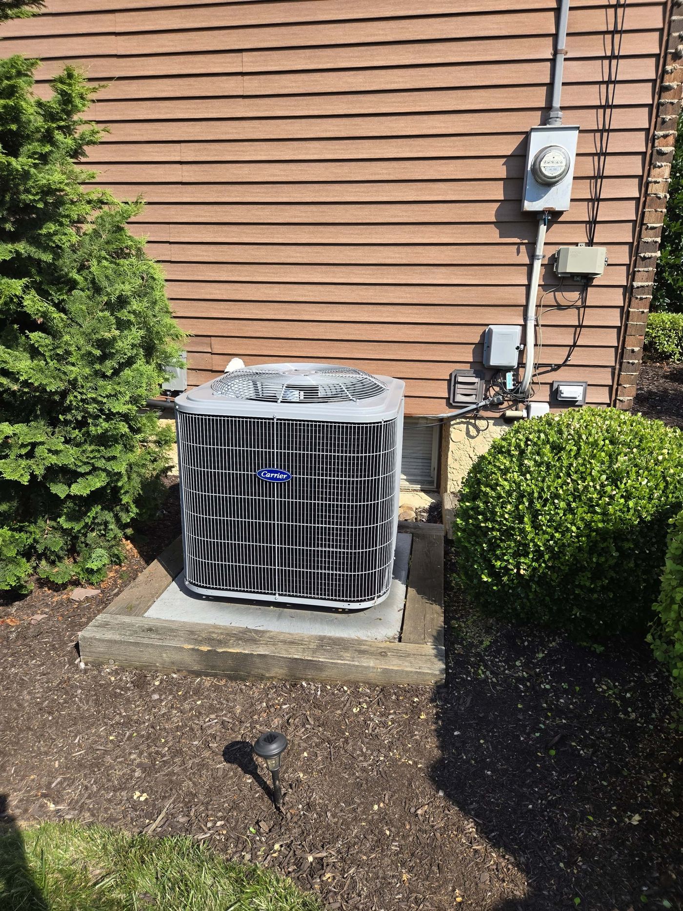 Carrier Air Conditioner condenser unit on a concrete slab outside a home on a sunny day.