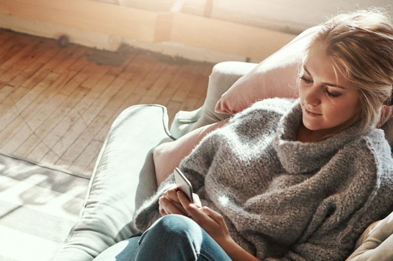 Shot of a young woman relaxing on the sofa at home and using a mobile phone