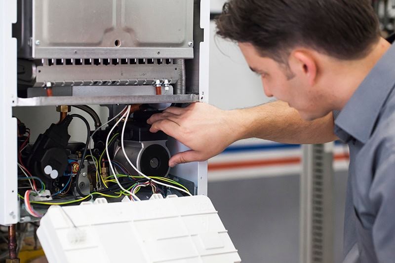 4 Important Heat Pump Maintenance Tips. An HVAC professional looking at a heat pump.
