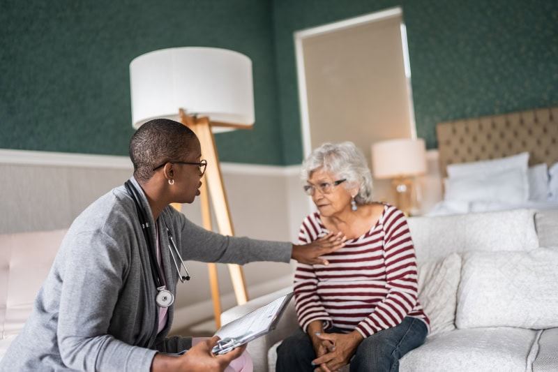 How Your HVAC Equipment Protects Against Viruses. Doctor talking to a senior woman in the bedroom.