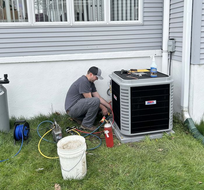 A KO HVAC technician servicing an outdoor condenser with gauges connected