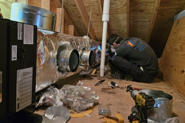 A KO HVAC technician fitting duct collars in an attic