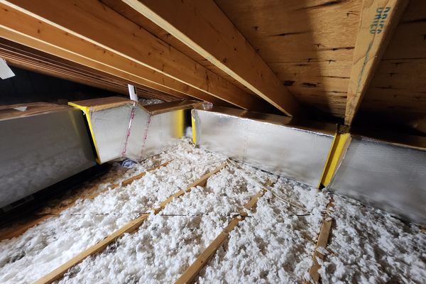 Insulated sheet-metal duct runs over blown insulation in an attic