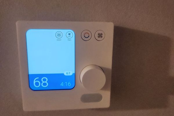 A wall thermostat with a dial and a backlit display reading 68