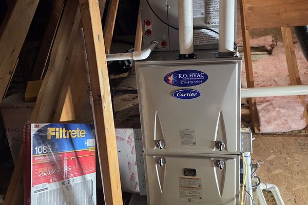 A Carrier furnace with a KO HVAC plate in an attic, a Filtrete filter beside it