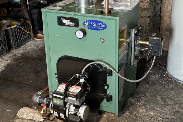 A green boiler with an oil burner and a KO HVAC sticker in a basement