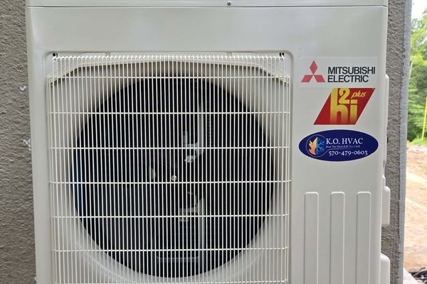 A Mitsubishi outdoor unit with the KO HVAC oval label on a stucco wall