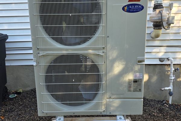 A two-fan Mitsubishi outdoor unit with a KO HVAC label on a steel stand