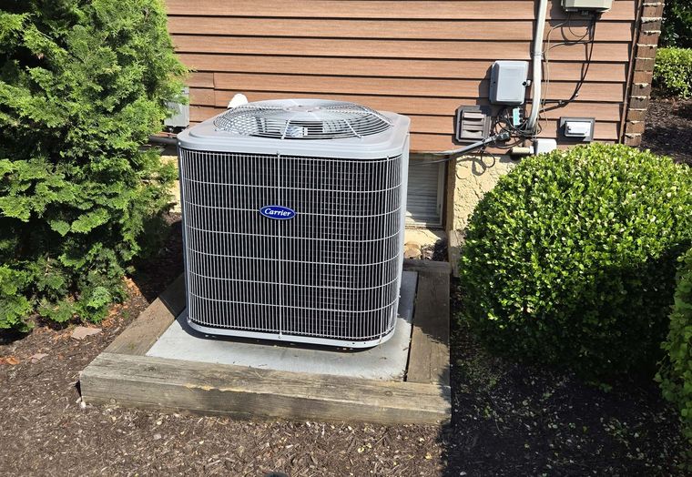 A new Carrier condenser on a concrete pad beside a house, next to a trimmed shrub