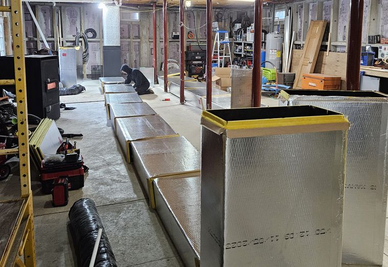 A long run of new insulated sheet-metal ductwork in a large basement