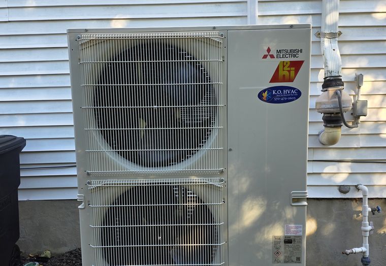 A two-fan Mitsubishi outdoor unit with a KO HVAC sticker on a raised stand