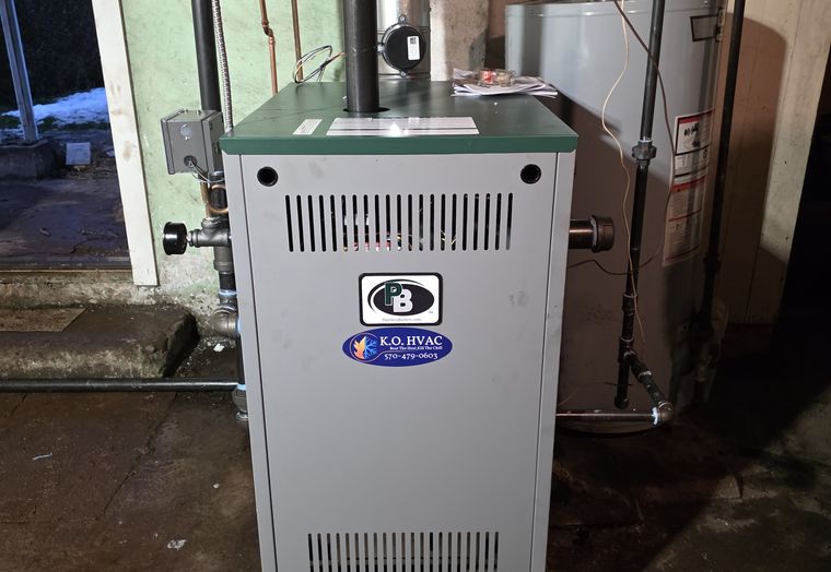 A gray boiler with a KO HVAC sticker in a basement