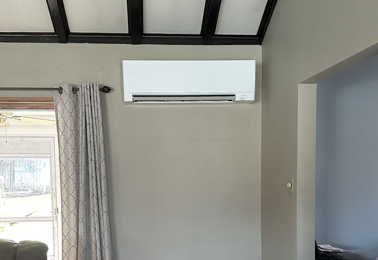 A Mitsubishi wall unit high on a living room wall below a beamed ceiling
