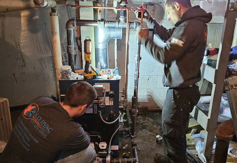 Two KO HVAC technicians working on a boiler in a basement