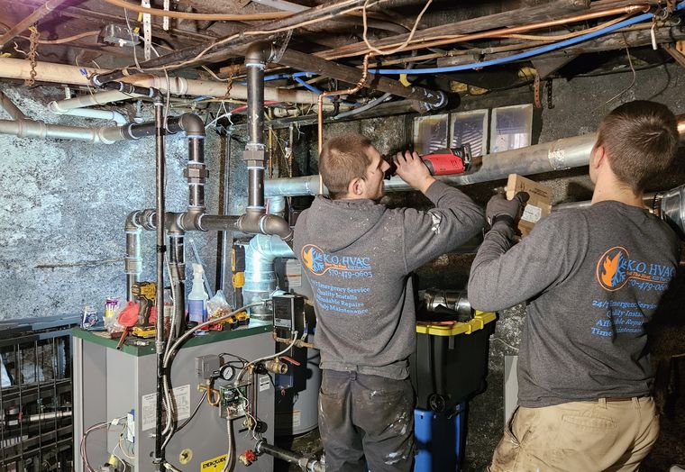 Two KO HVAC technicians in company shirts working in a boiler room