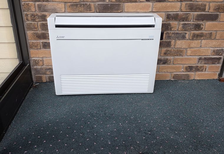 A floor-mounted Mitsubishi console unit in a sunroom against a brick wall