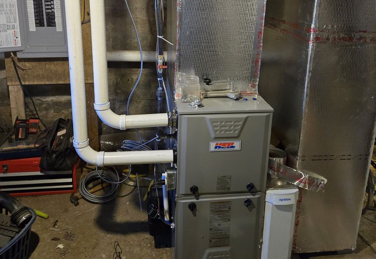 A furnace with a KO HVAC sticker and white venting in a basement