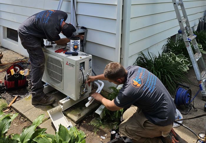 Two KO HVAC technicians installing an outdoor unit at the side of a house