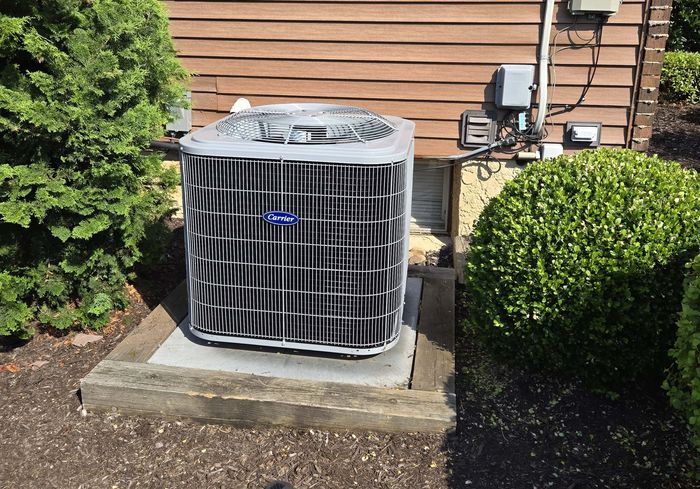 A new Carrier condenser on a concrete pad beside a house, next to a trimmed shrub