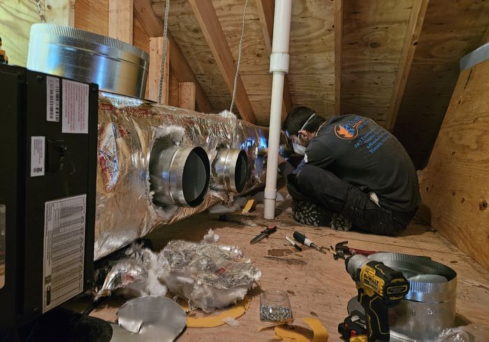 A KO HVAC technician fitting duct collars in an attic
