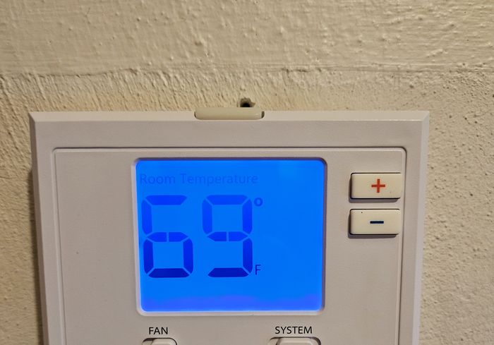 A wall thermostat with a blue backlit display reading 69 and a KO HVAC sticker