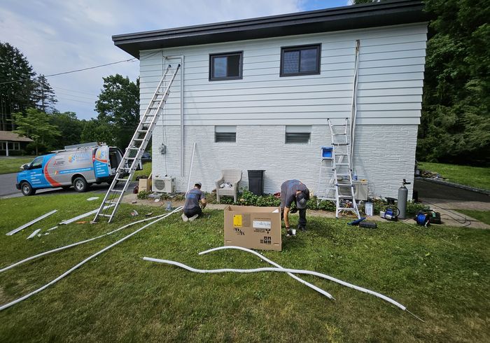 Two KO HVAC technicians installing outdoor units at a house, the KO van parked behind them