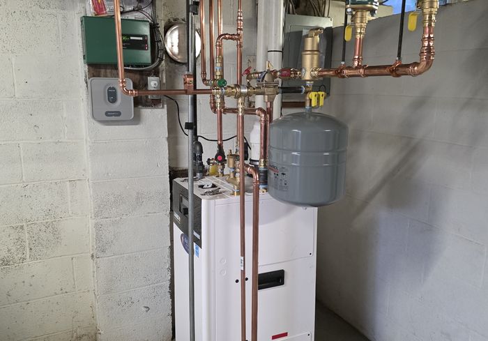 A white high-efficiency boiler with new copper piping and an expansion tank in a basement