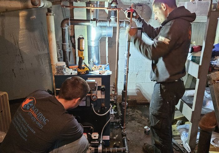 Two KO HVAC technicians working on a boiler in a basement