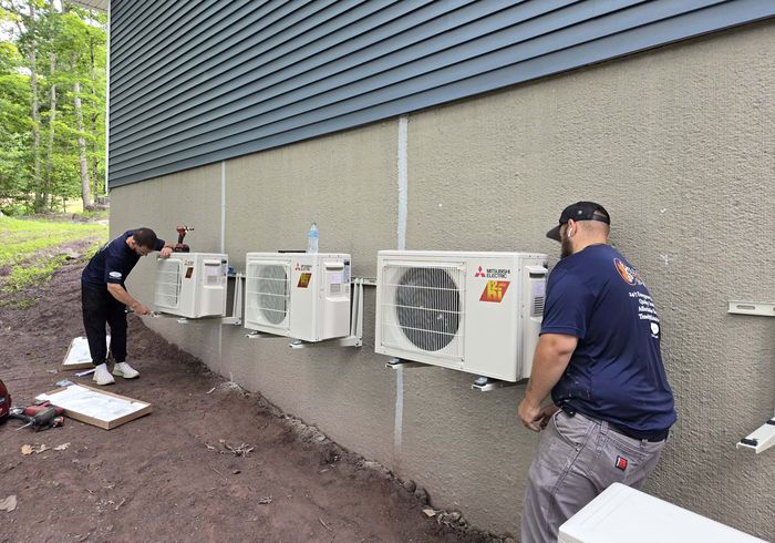 Two KO HVAC technicians mounting Mitsubishi mini-split outdoor units on a wall