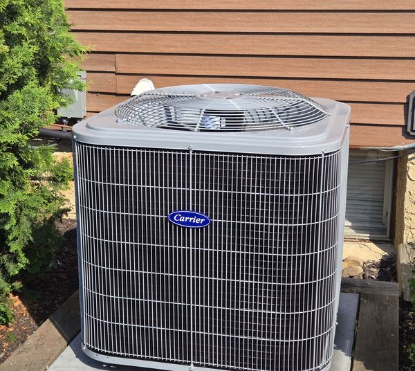 New Carrier air conditioner condenser on a pad beside a home