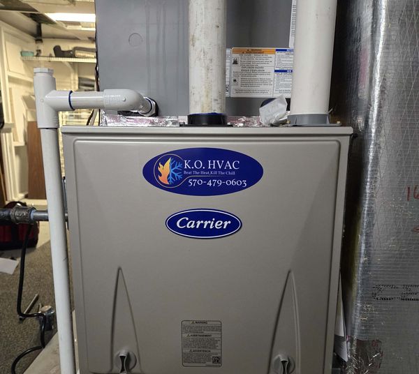 Carrier gas furnace with a KO HVAC sticker, installed in a basement
