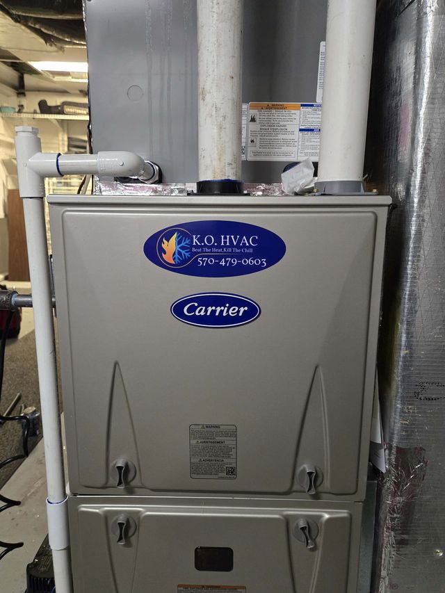 A Carrier gas furnace with a KO HVAC sticker, installed in a basement